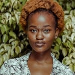 Portrait of a young woman with an afro hairstyle in front of vibrant green foliage.